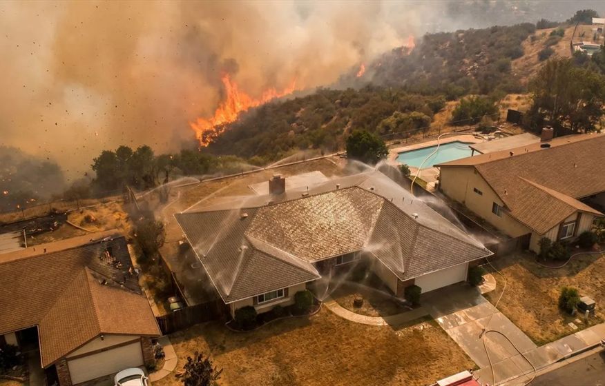 Wildfire home-defense concept showing roof sprinklers creating a protective water barrier